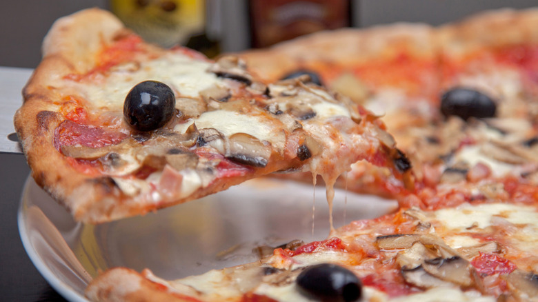 Pizza with pepperoni and olives, one slice being lifted