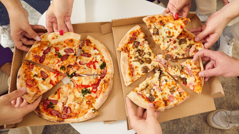 Top view of hands reaching for pizza slices in cardboard pizza boxes