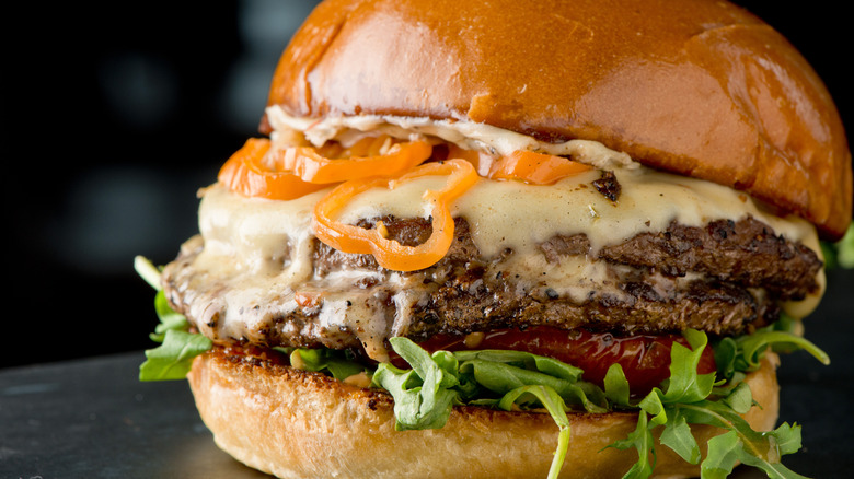 A closeup of a cheeseburger with sliced peppers and lots of cheese