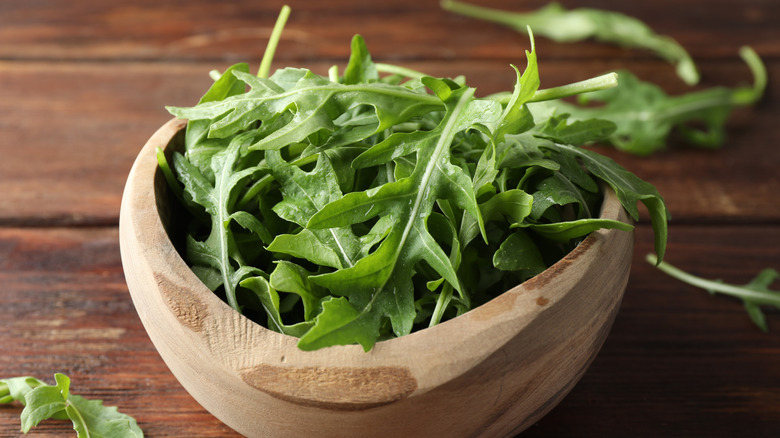 A wooden bowl of arugula on a table
