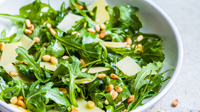 Arugula salad in a bowl with cheese shavings and pine nuts on top