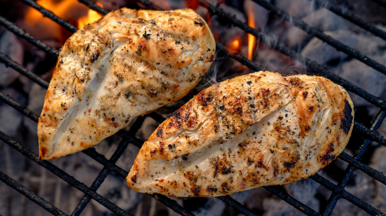 Two lightly-seasoned chicken breasts cooking on a grill.