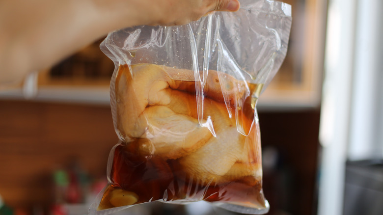 A person holding a plastic bag full of chicken brining in a brown liquid