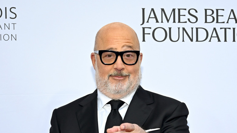 Andrew Zimmern attends the 2025 James Beard Restaurant and Chef Awards, wearing a suit, bold glasses, and watch while pointing at the camera.