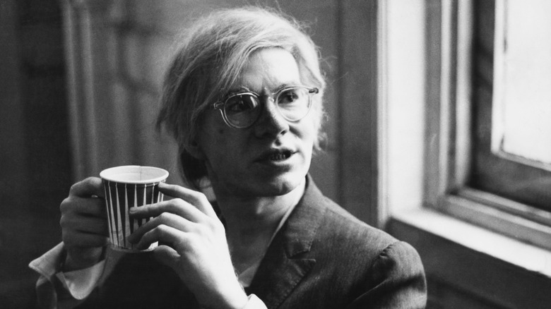 Black and white photo of Andy Warhol holding a paper cup
