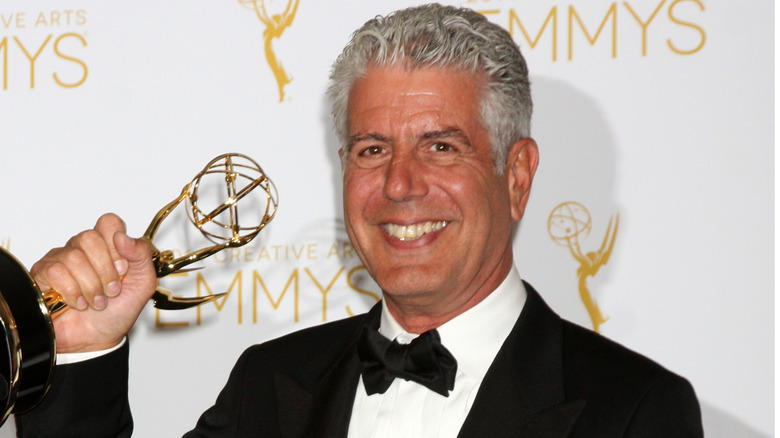 Anthony Bourdain smiles in a tuxedo while holding an Emmy