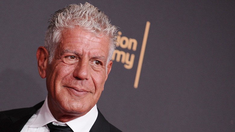 Anthony Bourdain smiling in a tuxedo while holding his Emmy Award on the red carpet