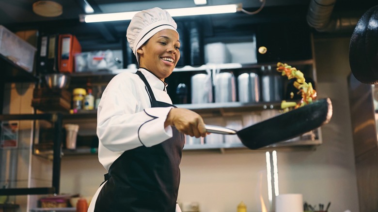 Smiling chef tossing food in frying pan