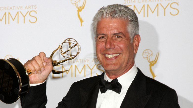 Smiling Anthony Bourdain in a tuxedo holding an Emmy Award
