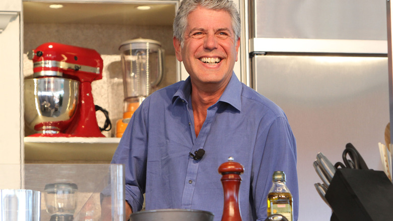 Anthony Bourdain smiling widely and wearing a blue shirt in a kitchen