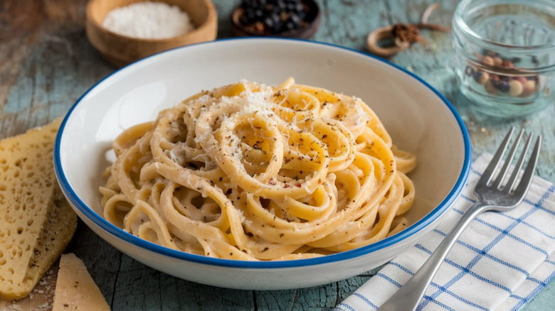 Spaghetti swirled in a white bowl with pepper flecks and cheese sprinkled on top with a fork next to it