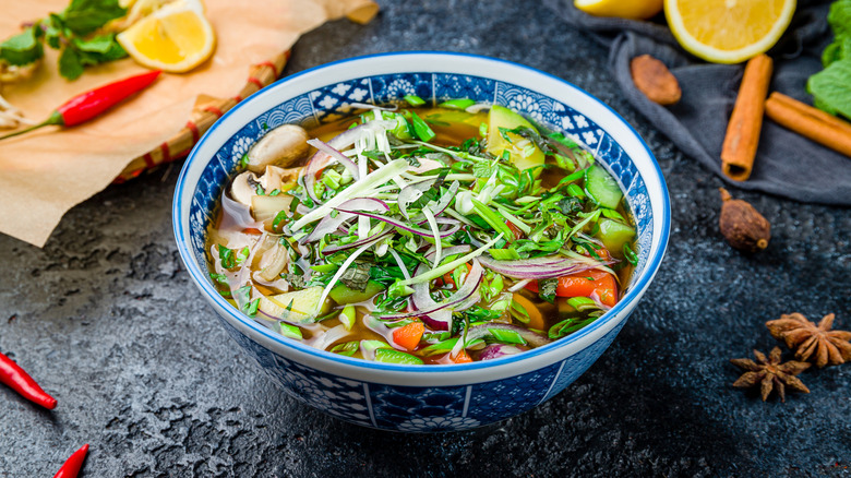 Pho soup with fresh herbs and veggies in a blue and white bowl with spices and seasonings