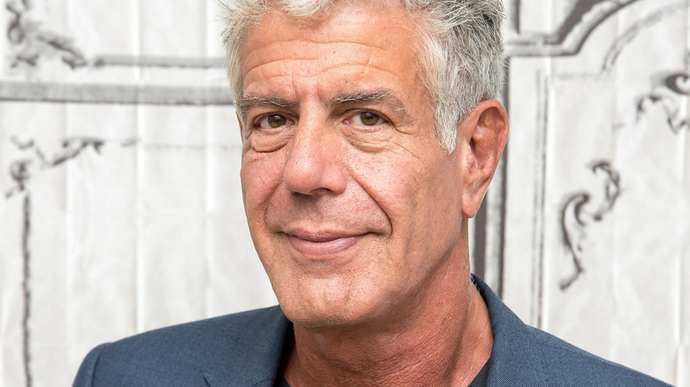 Anthony Bourdain smiles in a gray suit at a press event