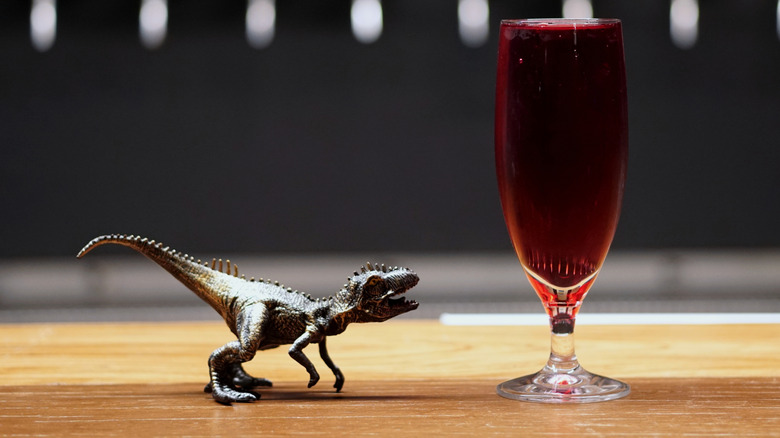 A dinosaur toy looking up at a glass of beer