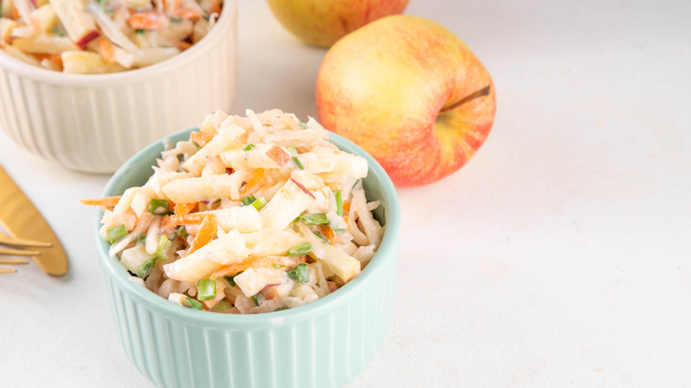Apple coleslaw in two ramekins side by side with whole apples nearby.