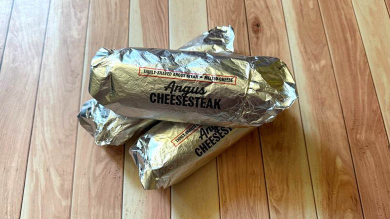 Angus cheesesteak sandwiches from Arby's wrapped in branded foil wrappers on table
