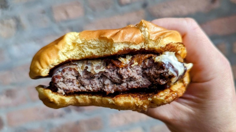 A person holding a half-eaten Big Game Burger from Arby's.