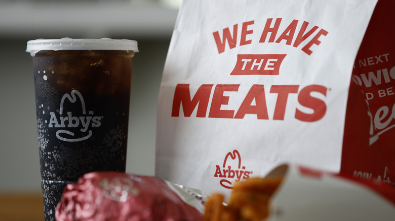 Arby's meal displayed on table with bag, sandwich, fries, drink.