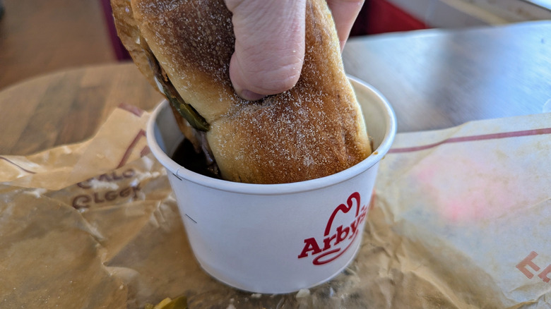 hand dunking sandwich into jus