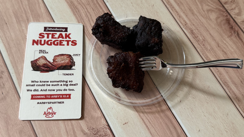 A few Steak Nuggets on a plate with a fork and an Arby's promotional card