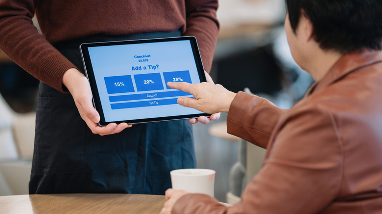 Person holding up IPad with tip screen for another person to select a tip