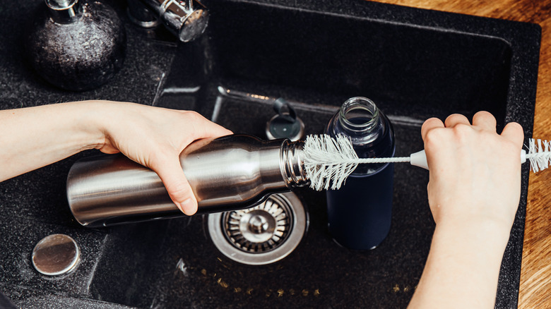 Cleaning reusable water bottle in kitchen sink with bottle brush