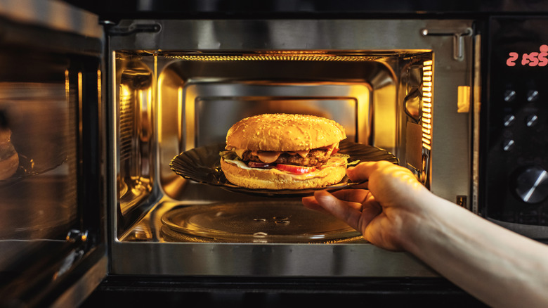 Someone placing a cheeseburger on a plate in the microwave.
