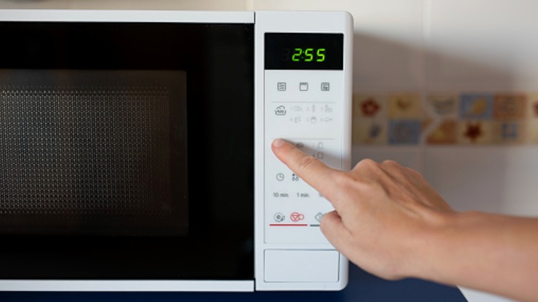 Hand pressing a button on a microwave oven.