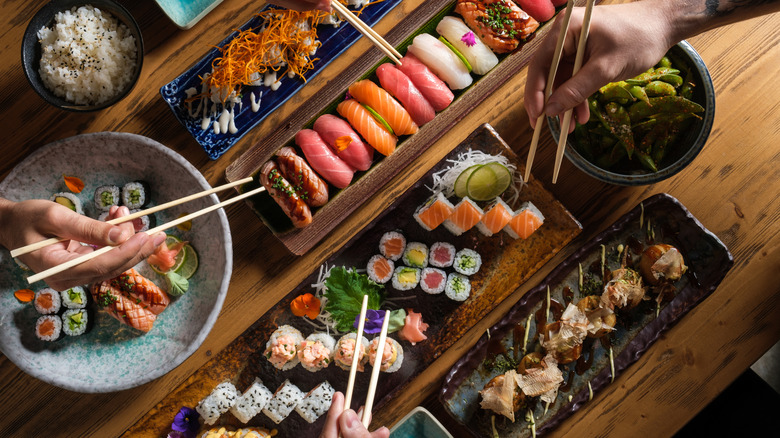 Hands holding chopsticks and hovering over a selection of different types of sushi
