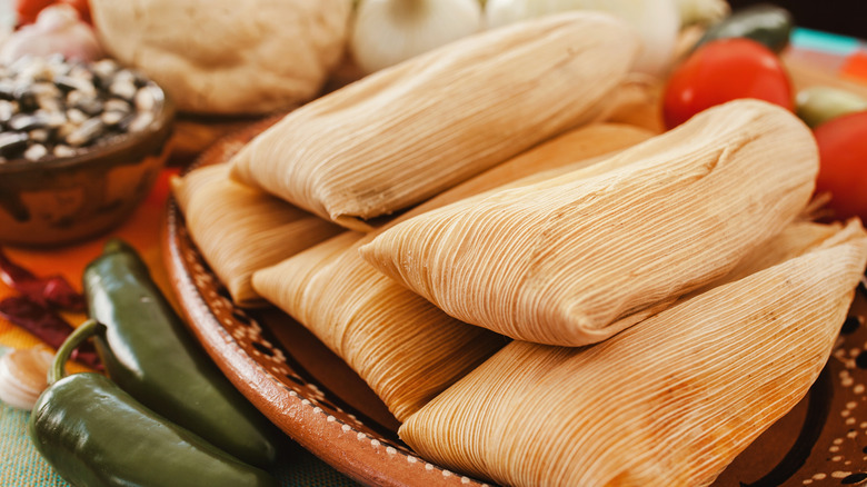 Tamales wrapped in corn husks on a brown plate