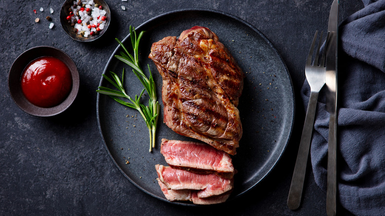 Medium rare steak on a black plate with rosemary sprig