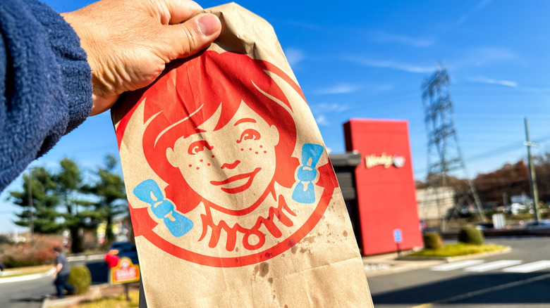 Hand holding a Wendy's takeout bag near a Wendy's location exterior