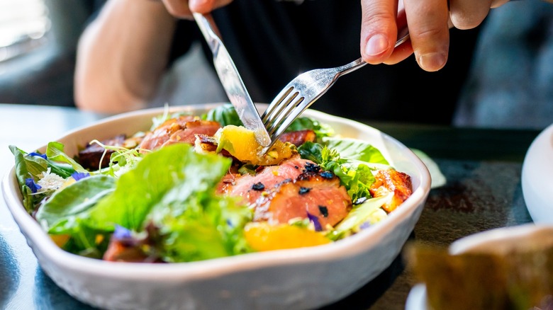 Person eating salad with fork and knife close up