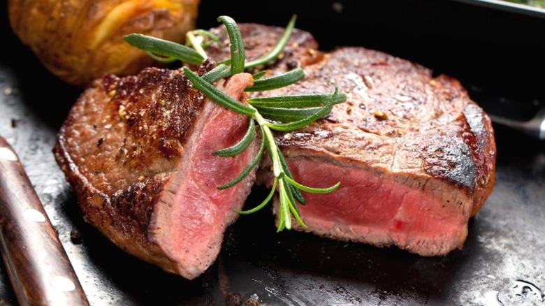 A rare steak, halved and topped with rosemary, next to a potato
