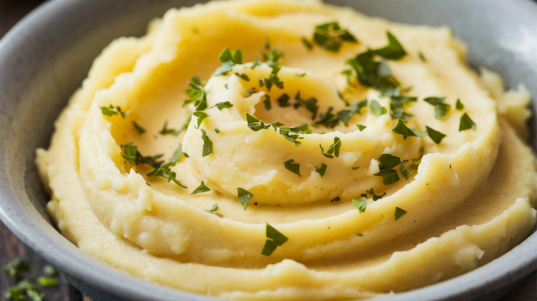 A bowl of mashed potatoes in an aesthetic swirl with green herbs sprinkled on top