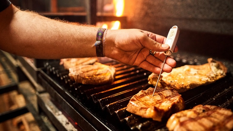 Chef using a thermometer to check meat on a grill