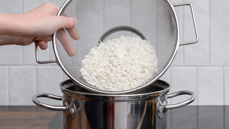 A person adds rinsed white rice from a colander to a pot