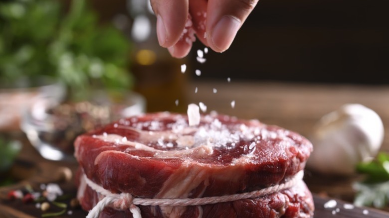 A hand seasons a raw piece of steak.