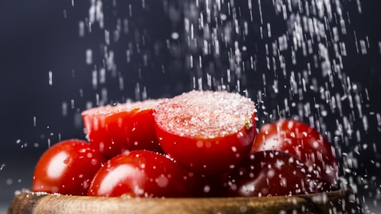 Salt rains down on a stack of tomato halves.