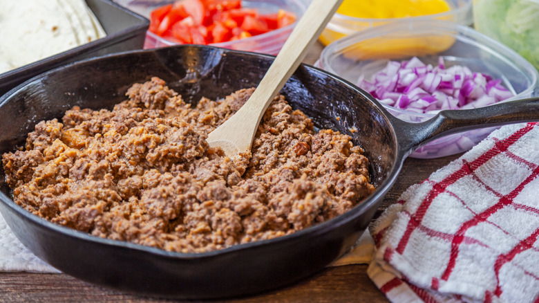 ground beef in a pan off the stove next to the obligatory checked towel