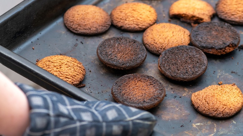 Person pulling burnt cookies on sheet pan from oven