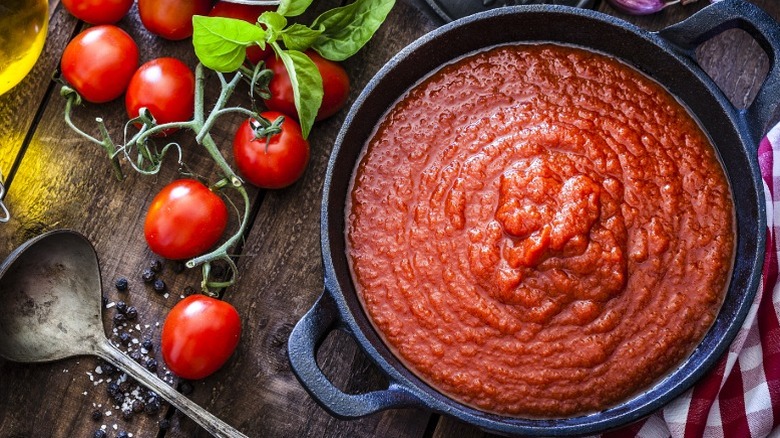A pot of tomato sauce next to a ladle, tomatoes, and olive oil.