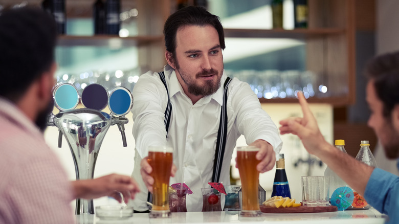 Two guys speaking to a bartender as he gives them their glasses of beer.