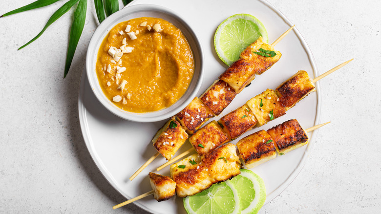 Grilled tofu satay skewers and peanut spicy sauce on white plate close up