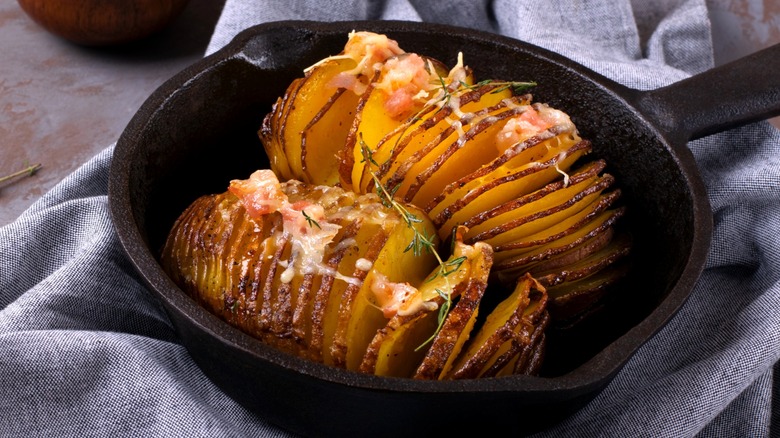 Hasselback potatoes topped with herbs and cheese in a cast iron skillet