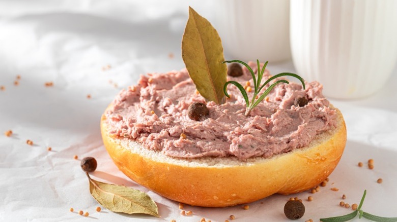 A half of a roll with meat spread and herbs atop it