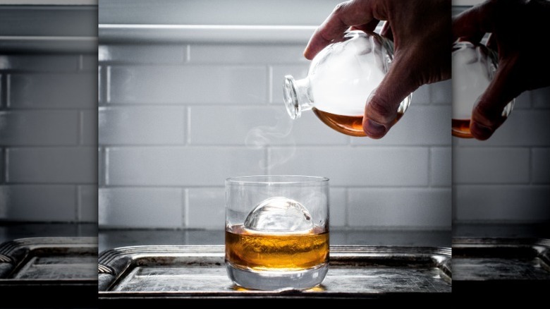 pouring whiskey over an ice sphere
