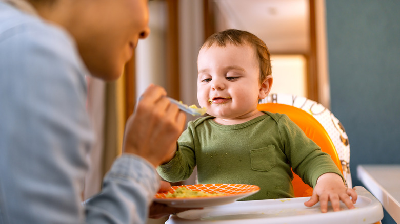Baby sitting in high chair being fed