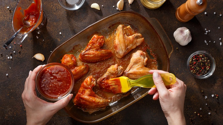 Person brushing BBQ sauce onto baked chicken wings