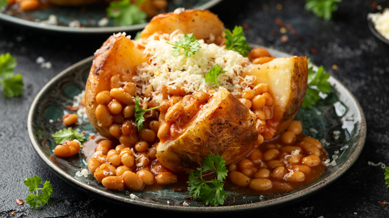 A baked potato topped with steaming baked beans and cheddar cheese on a white plate